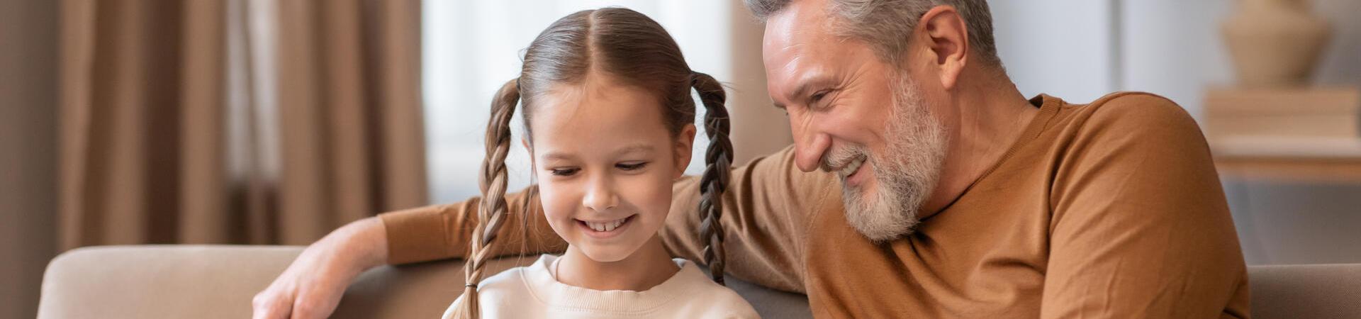 Vater sitzt mit seiner Tochter auf dem Sofa und schaut gemeinsam mit ihr auf ein Smartphone