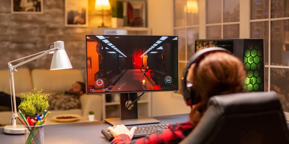 Person sitzt in einem Gaming-Stuhl und spielt ein Action-Spiel an einem PC, der Monitor zeigt das Spielgeschehen
