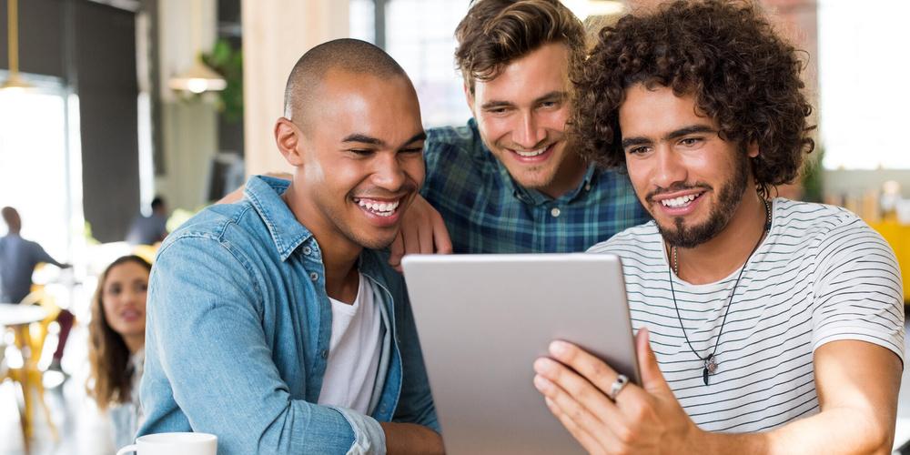 Drei Personen schauen gemeinsam auf ein Tablet an einem Tisch