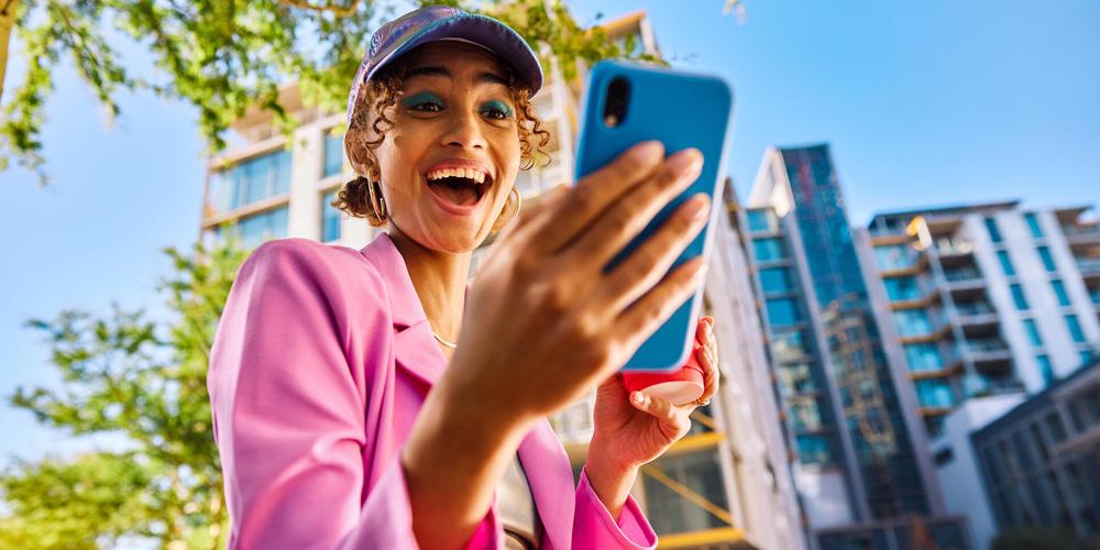 Frau schaut lachend auf ein Smartphone in ihrer Hand