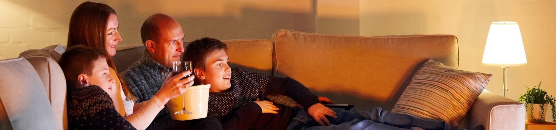 Familie sitzt abends gemeinsam auf dem Sofa und schaut entspannt einen Film oder eine Serie.