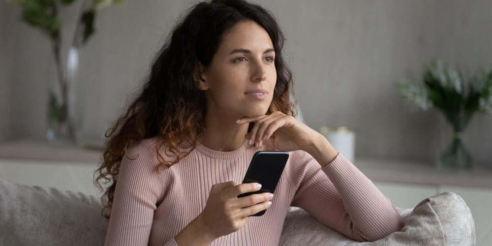 Frau sitzt auf einem Sofa und hält ein Smartphone in der Hand