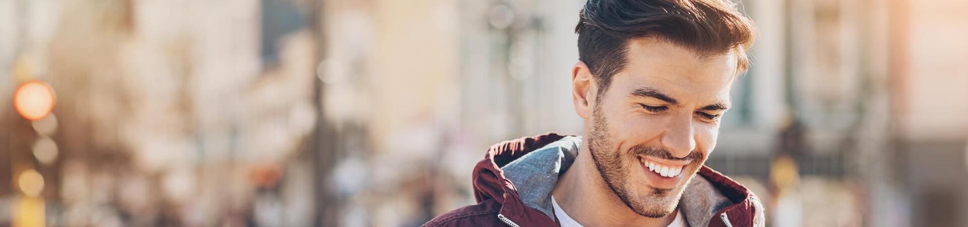 Ein junger Mann steht in einer Einkaufsstraße und blickt fröhlich auf sein Smartphone