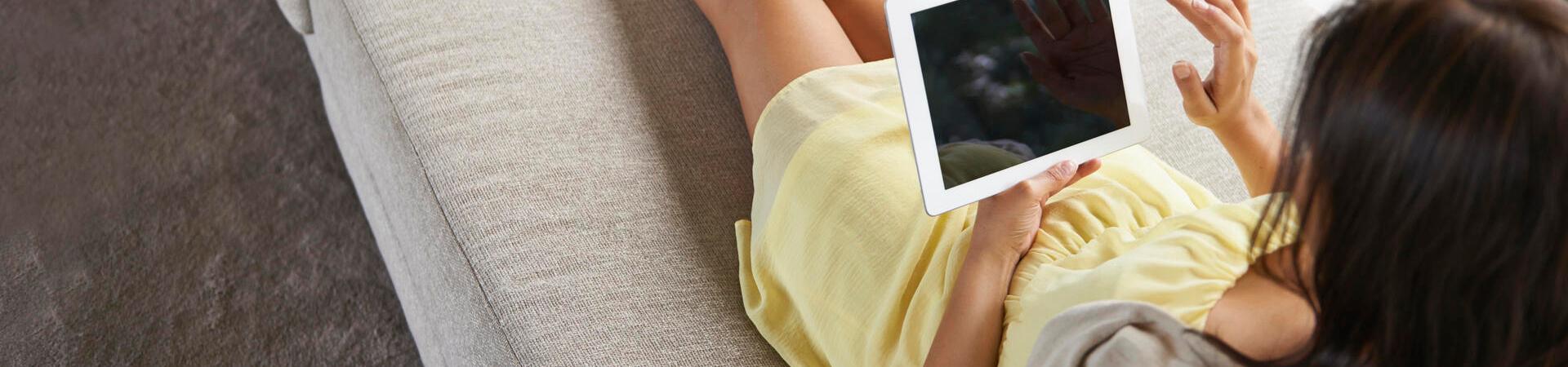 Frau liegt auf einem Sofa mit einem Tablet in der Hand