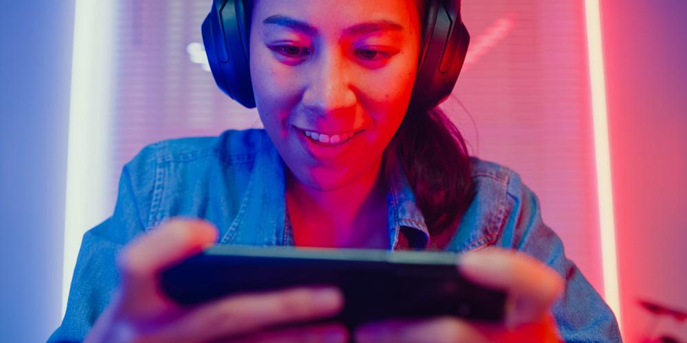 Nahaufnahme einer jungen asiatischen Frau, die ein Online-Smartphone-Videospiel spielt und das Streaming live im Neonlicht-Wohnzimmer zu Hause überträgt.
