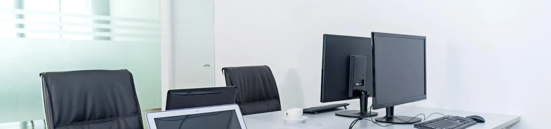 Heller Büroraum mit Laptop, zwei Monitoren und mehreren Arbeitsplätzen