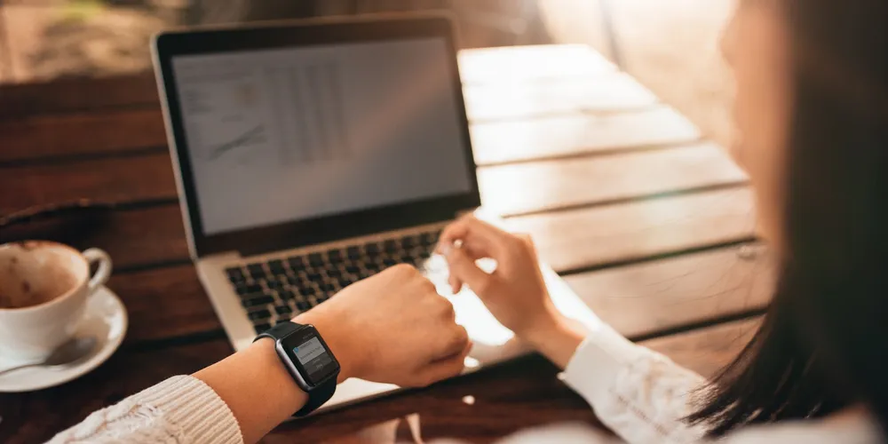 Person arbeitet am Laptop und prüft eine Nachricht auf der Smartwatch