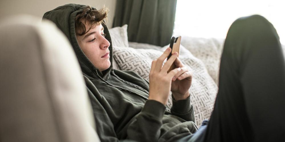 Jugendlicher liegt mit einem Smartphone in der Hand auf dem Sofa