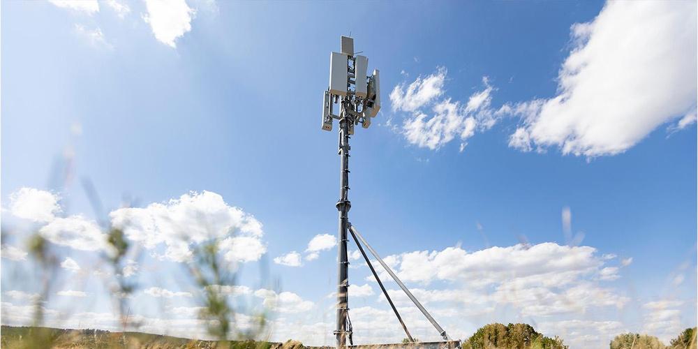 Mobilfunkmast mit Antennen in ländlicher Umgebung vor blauem Himmel mit Wolken 