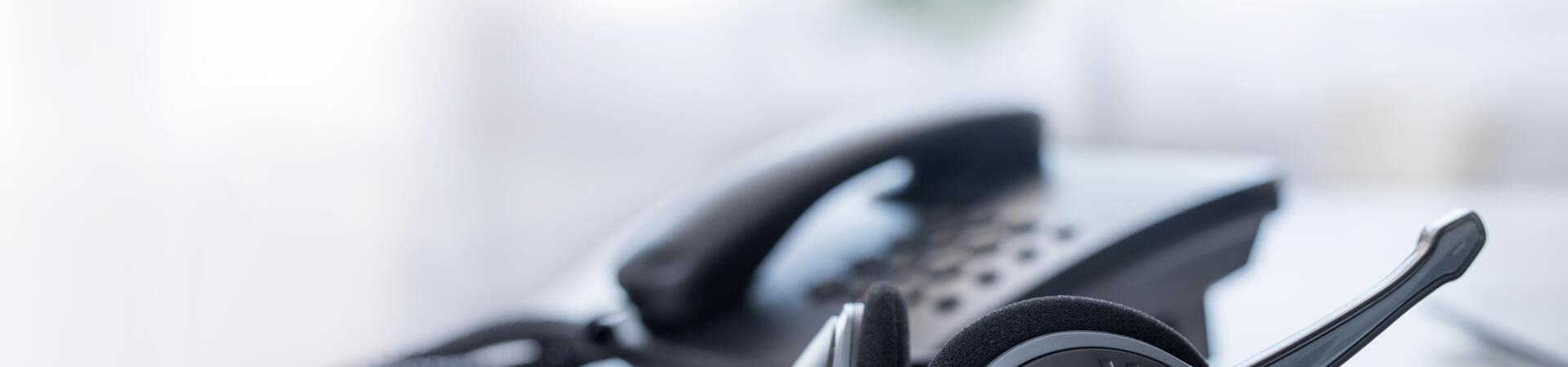 Ein an ein Kabeltelefon angebundenes Headset liegt auf einem weißen Tisch
