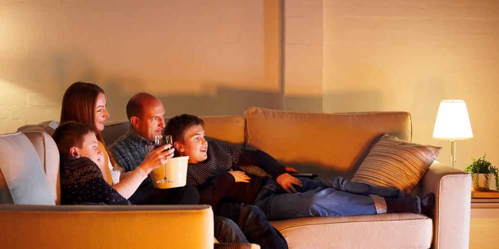 Familie sitzt abends gemeinsam auf dem Sofa und schaut entspannt einen Film oder eine Serie.