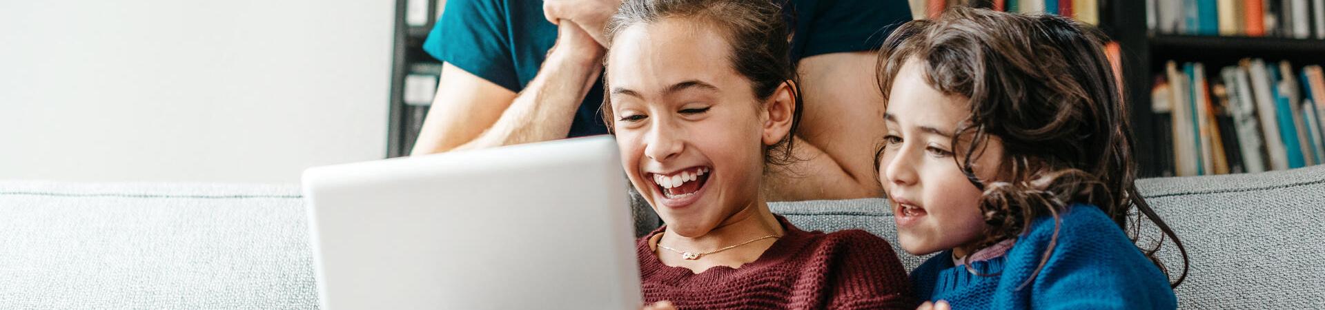 Vater und zwei Kinder sitzen auf dem Sofa und schauen gemeinsam auf ein Tablet