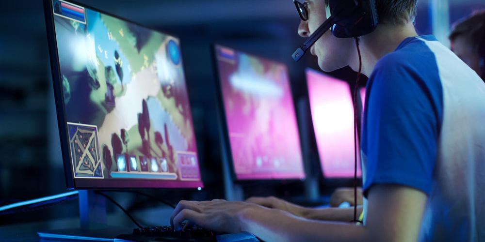 Junger Gamer mit Headset spielt an mehreren Monitoren ein Online-Videospiel