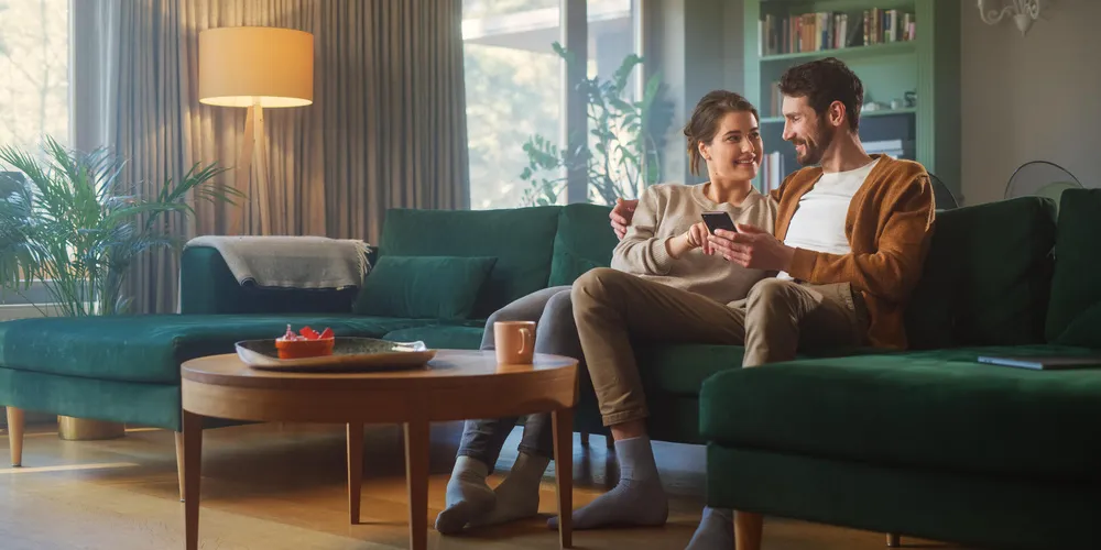 Ein Paar nutzt gemeinsam ein Smartphone in einem modern eingerichteten Wohnzimmer