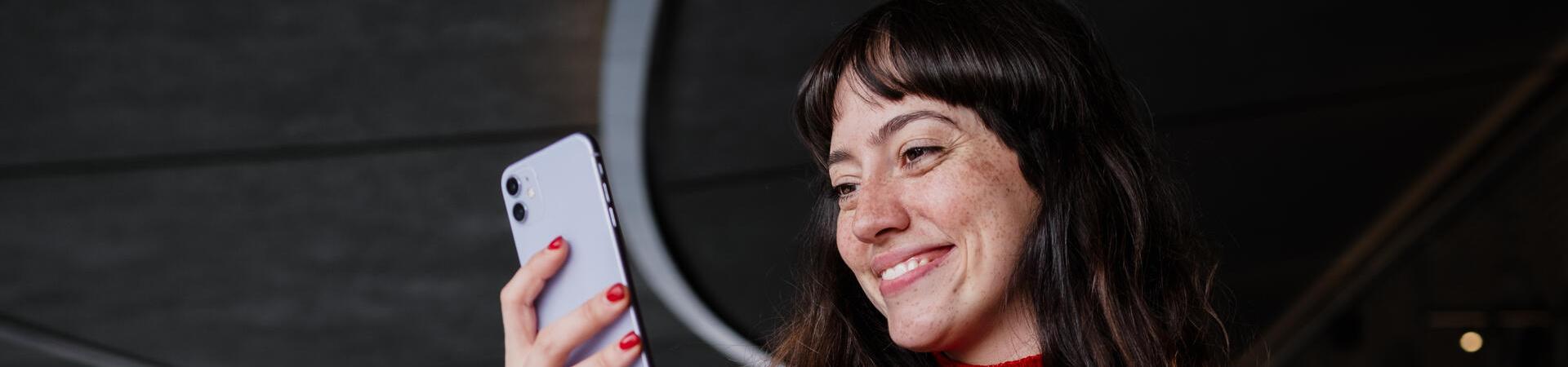 Frau im roten Pullover schaut lächelnd auf ein Smartphone