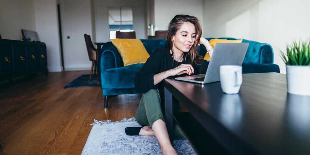 Frau sitzt im Wohnzimmer am Couchtisch und arbeitet an einem Laptop