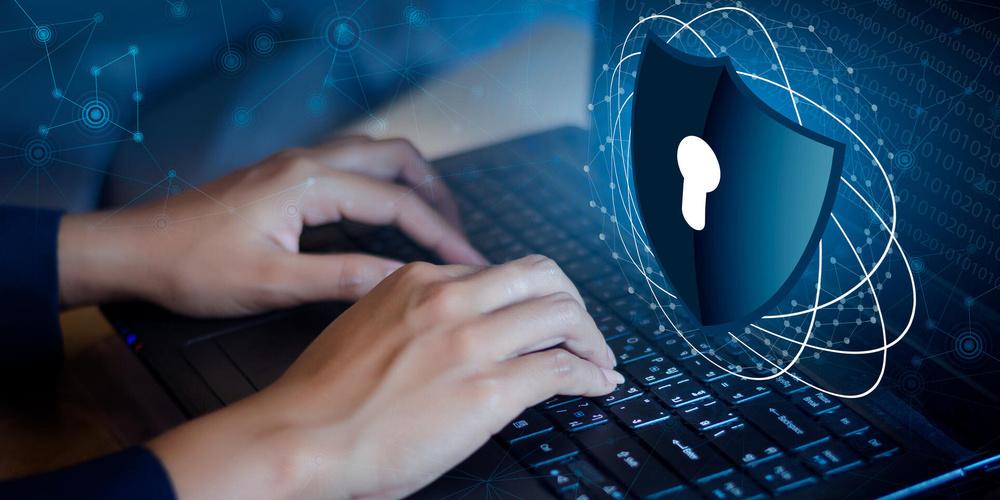 Hände tippen auf einer Laptop-Tastatur, darüber ein digitales Schutzschild-Symbol mit Schlüsselloch