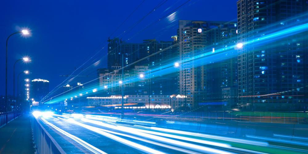 Nächtliche Stadtstraße mit Lichtspuren fahrender Autos und beleuchteten Hochhäusern