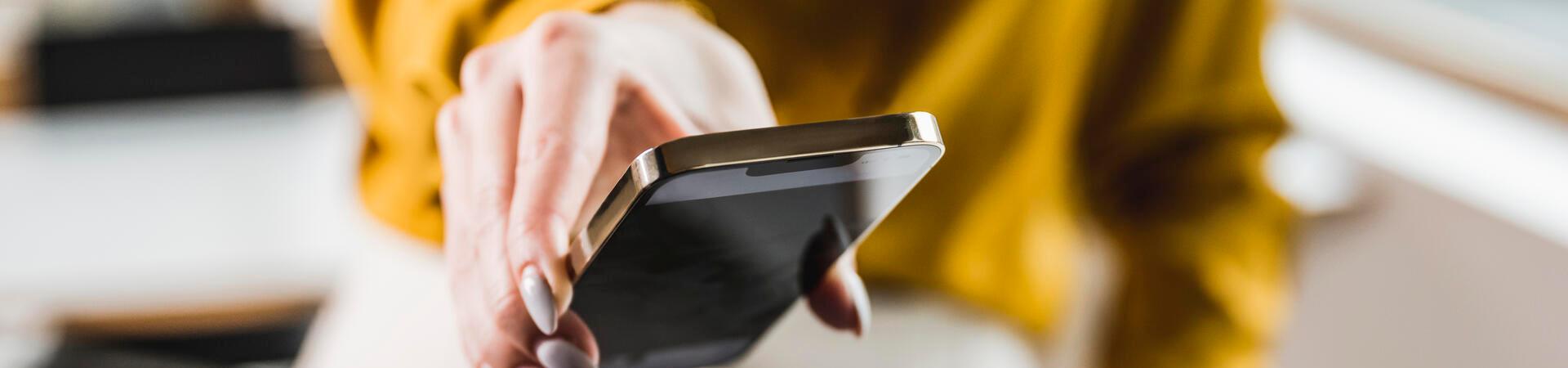 Eine Person hält ein Smartphone über ein Kartenterminal und bezahlt kontaktlos an der Kasse