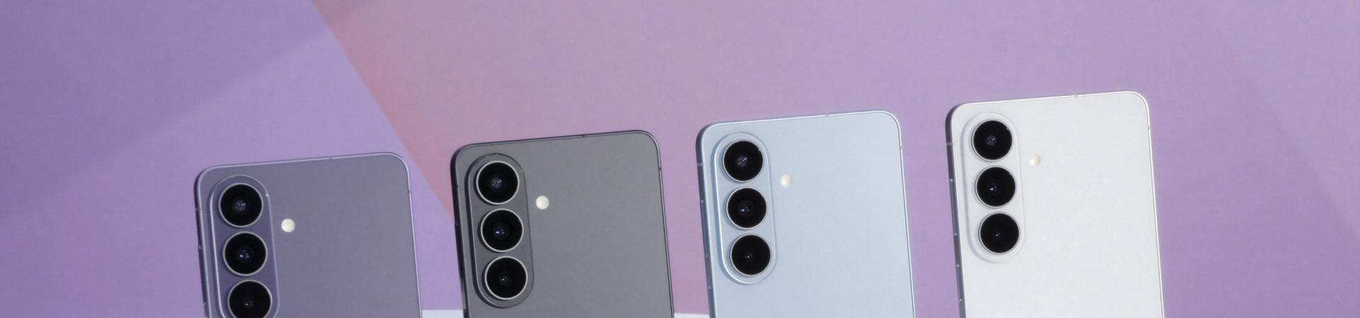Vier Samsung-Smartphones in Lila, Grau, Hellblau und Weiß nebeneinander auf einer weißen Fläche vor einem hellvioletten Studiohintergrund