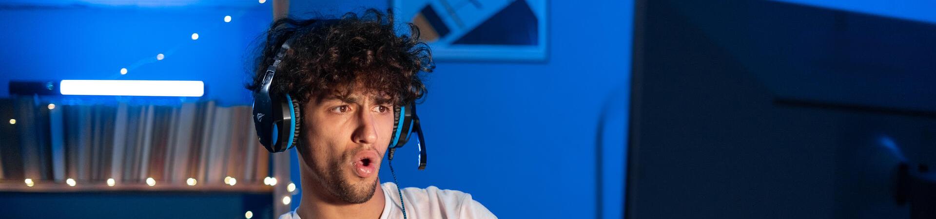 Gamer spielt zu Hause am PC mit Headset und großem Monitor
