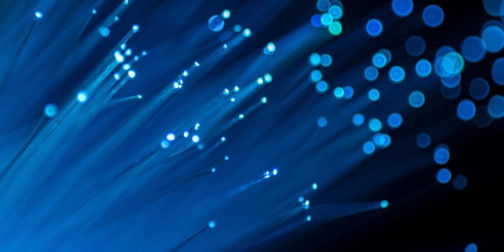 Nahaufnahme von Glasfasern mit leuchtenden blauen Lichtpunkten
