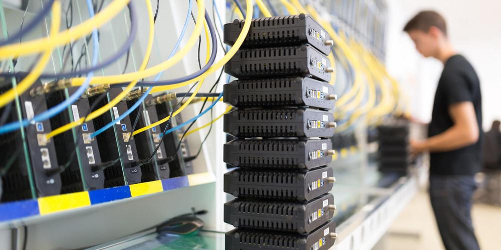 Server Rack mit entsprechender Verkabelung; im Hintergrund arbeitet ein Mensch an weiteren Bauteilen