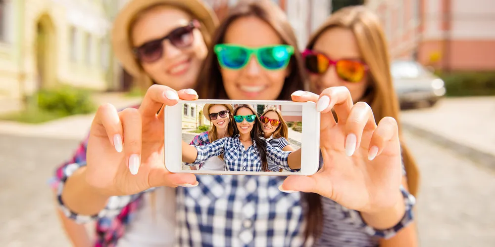 Drei Personen fotografieren sich mit einem Smartphone auf einer Straße