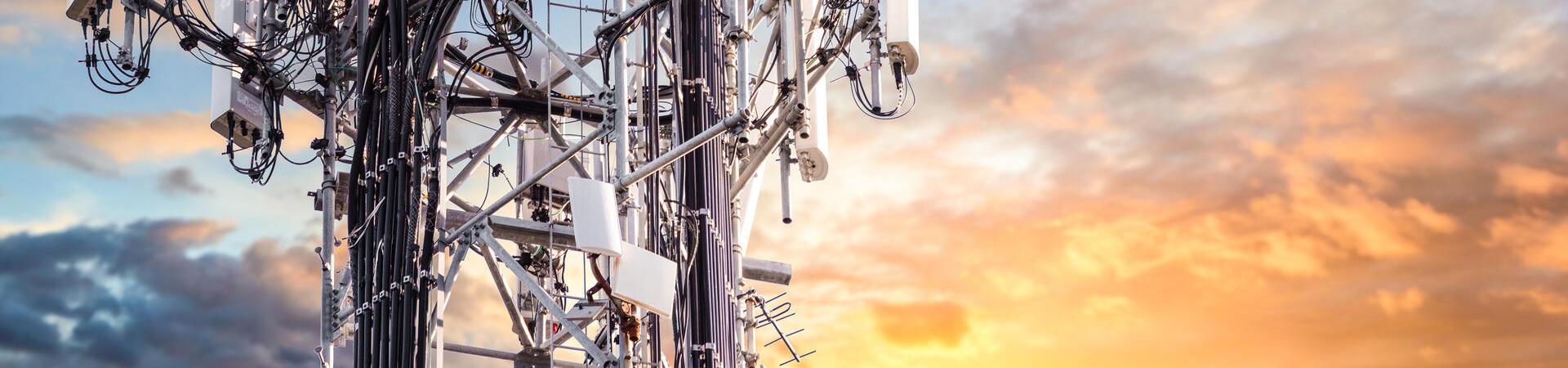 Mobilfunkmast mit mehreren Antennen vor Himmel bei Sonnenuntergang