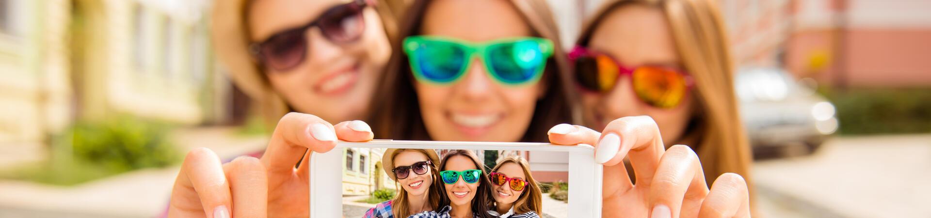 Drei Personen fotografieren sich mit einem Smartphone auf einer Straße