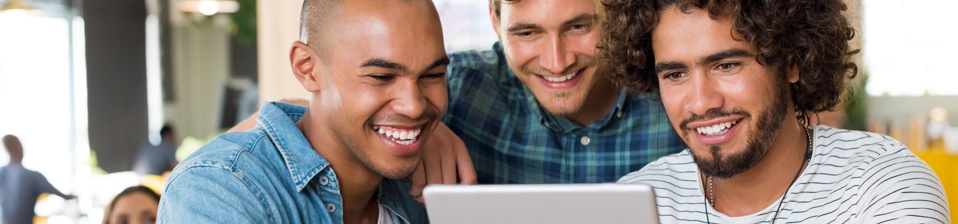Drei Personen schauen gemeinsam auf ein Tablet an einem Tisch