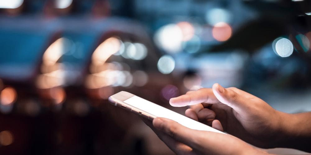 Hände bedienen ein leuchtendes Smartphone vor unscharfem nächtlichem Stadtverkehr mit Bokeh-Lichtern im Hintergrund