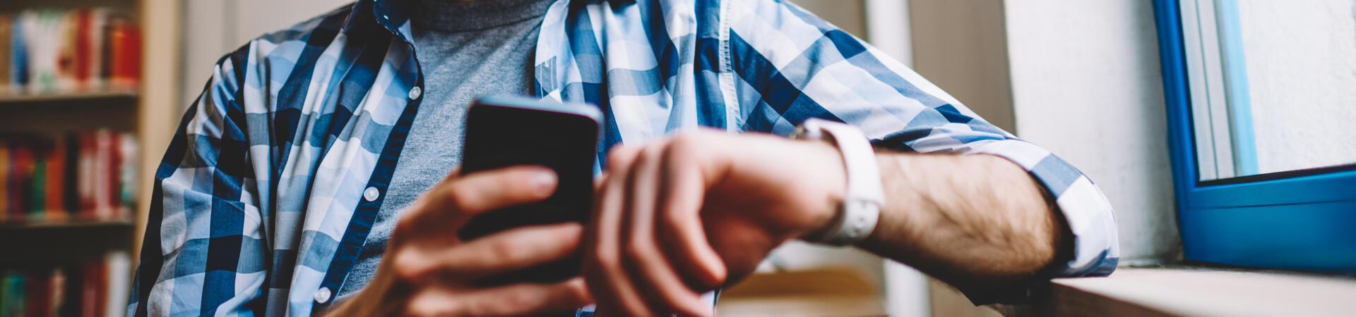 Person mit Brille schaut auf eine Smartwatch und hält ein Smartphone in der Hand