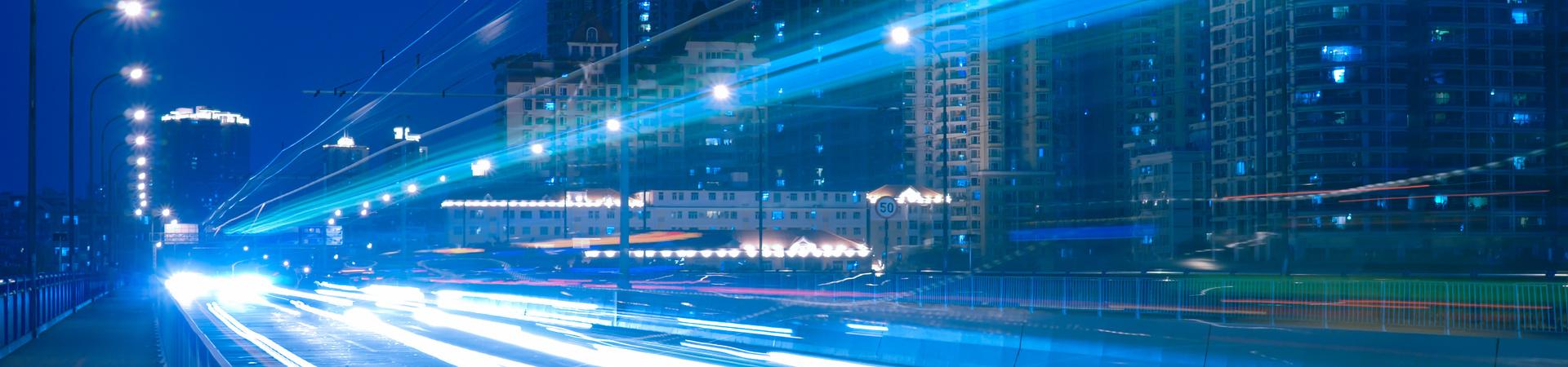 Nächtliche Stadtstraße mit Lichtspuren fahrender Autos und beleuchteten Hochhäusern