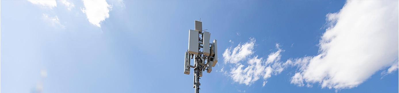 Mobilfunkmast mit Antennen in ländlicher Umgebung vor blauem Himmel mit Wolken
