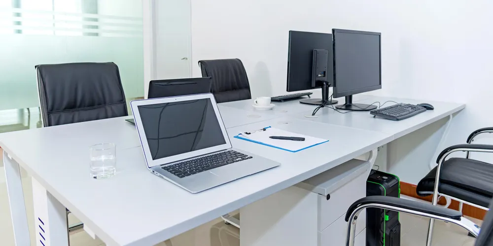 Heller Büroraum mit Laptop, zwei Monitoren und mehreren Arbeitsplätzen