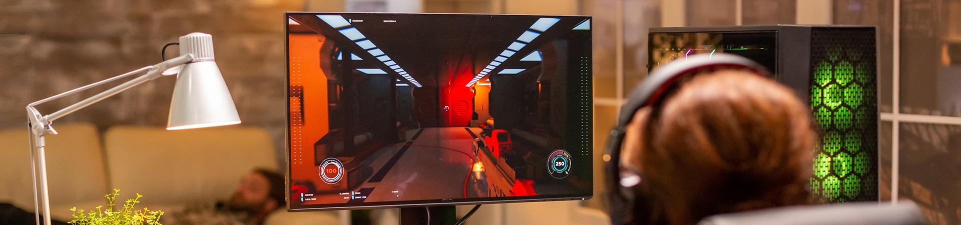 Person sitzt in einem Gaming-Stuhl und spielt ein Action-Spiel an einem PC, der Monitor zeigt das Spielgeschehen