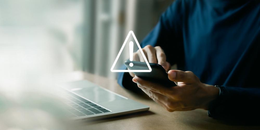 Person nutzt ein Smartphone und ein Warnsymbol über dem Display zeigt eine Internetstörung an
