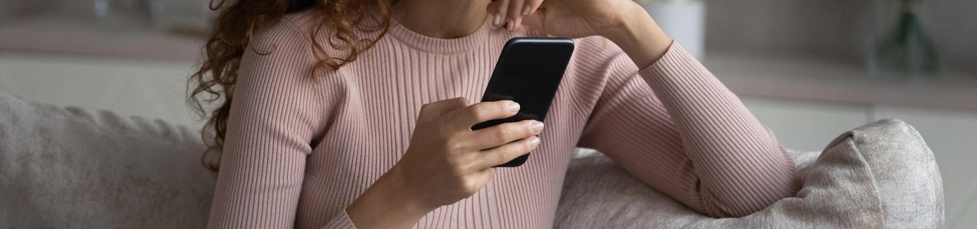 Frau sitzt auf einem Sofa und hält ein Smartphone in der Hand