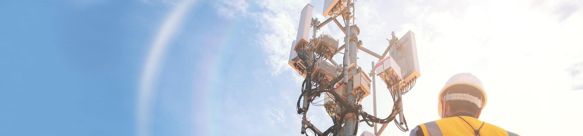 Ein Techniker in Warnweste blickt zu einem Funkmast hoch