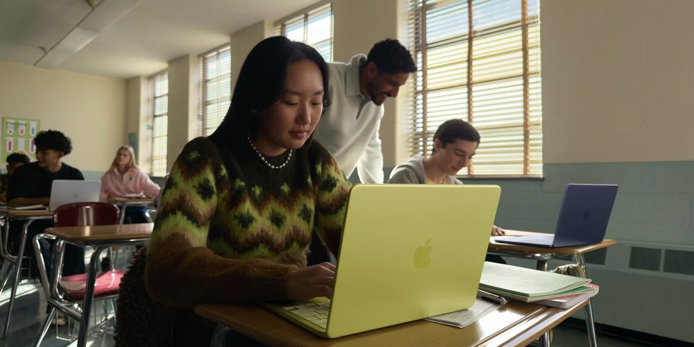 Eine Schülerin sitzt im Klassenzimmer an ihrem Tisch vor einem zitrusfarbenen MacBook Neo