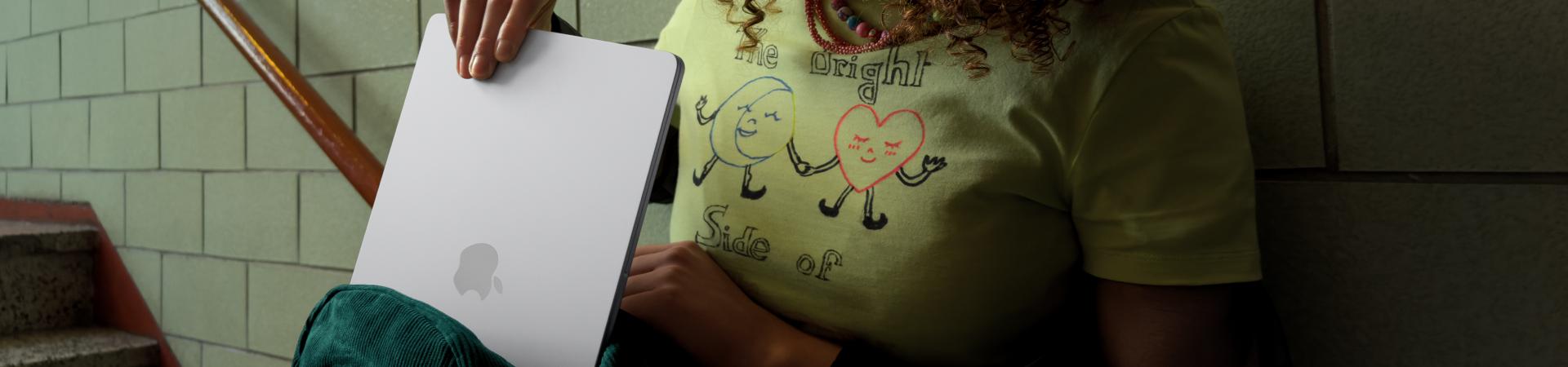 Frau sitzt auf einer Treppe und nimmt ein MacBook Air aus einer grünen Tasche