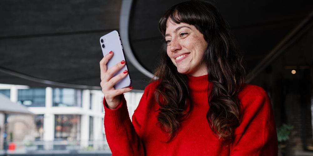 Frau im roten Pullover schaut lächelnd auf ein Smartphone