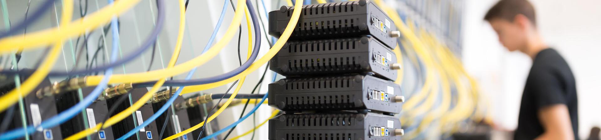 Server Rack mit entsprechender Verkabelung; im Hintergrund arbeitet ein Mensch an weiteren Bauteilen