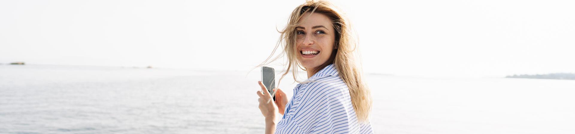 Frau sitzt auf einem Boot und hält ein Smartphone in der Hand