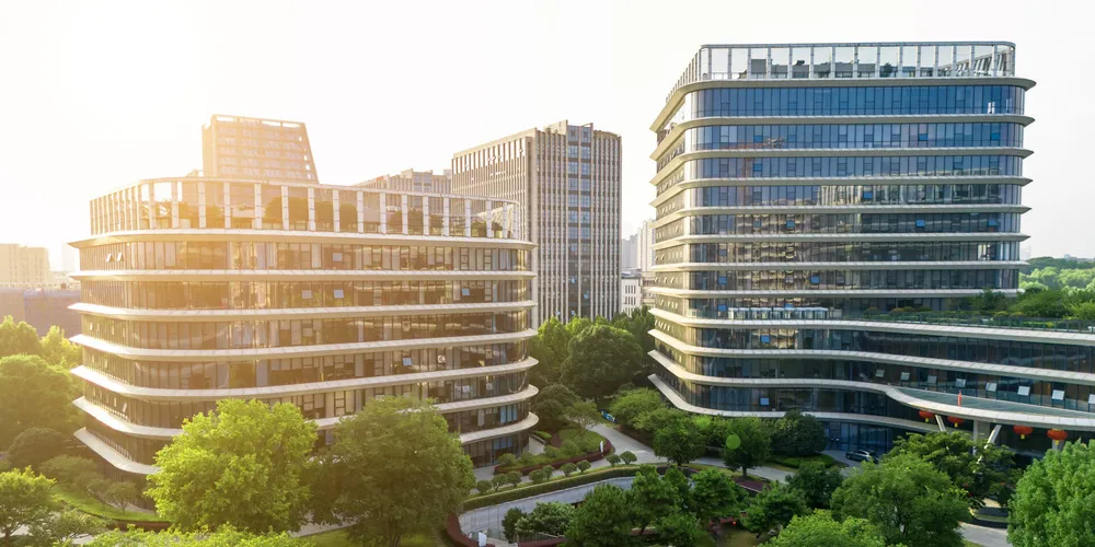 Moderne Gebäude mit Glasfassaden, umgeben von Grünflächen und Bäumen bei tief stehender Sonne