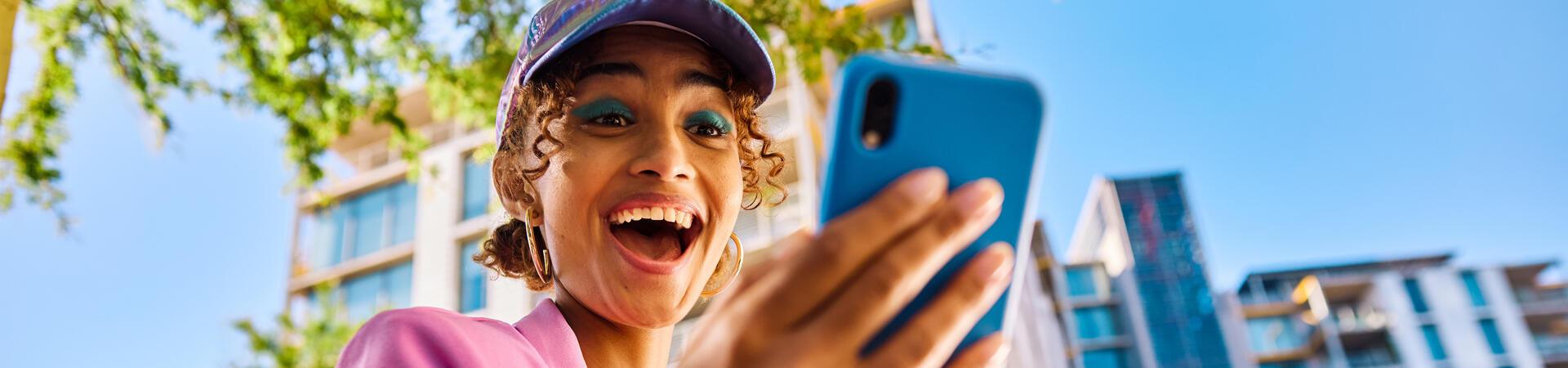 Frau schaut lachend auf ein Smartphone in ihrer Hand