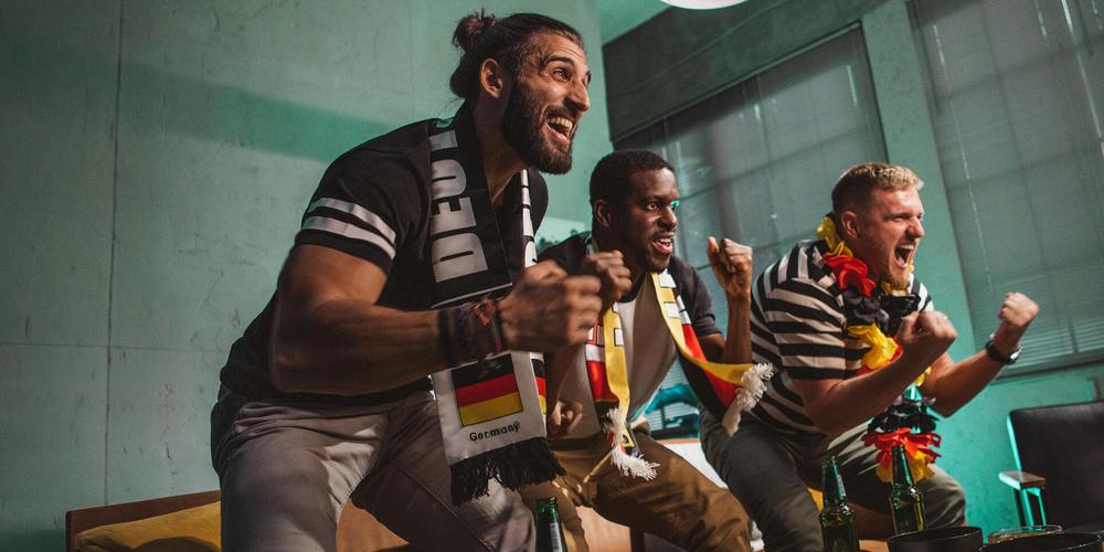 Drei Fußballfans jubeln in einem Wohnzimmer