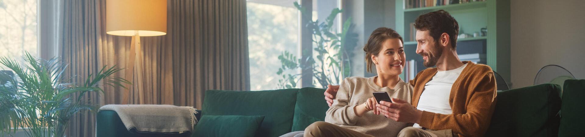 Ein Paar nutzt gemeinsam ein Smartphone in einem modern eingerichteten Wohnzimmer