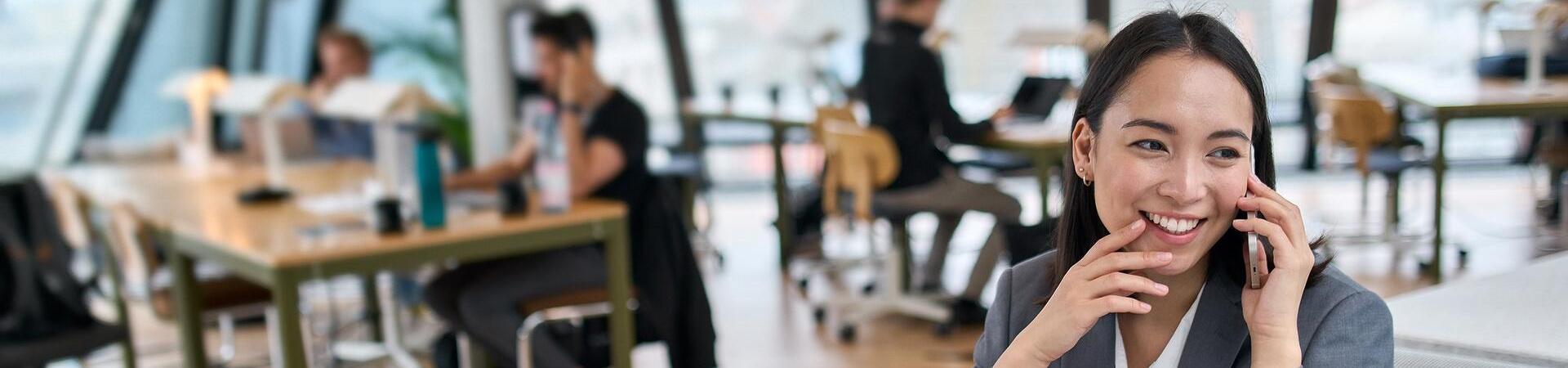 Eine Frau sitzt in einem Büro an ihrem Schreibtisch und telefoniert